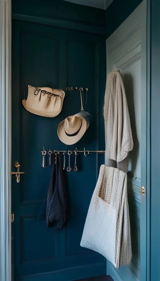 The back of a closet door organized with adhesive hooks holding a hat, bag, and cardigan.