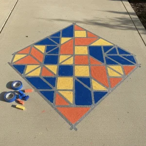 A colorful geometric tape resist mosaic created with sidewalk chalk on a clean concrete driveway.