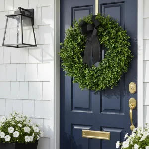 A dense, high-quality faux boxwood spring wreath for front door styled with a black grosgrain ribbon on a navy blue door.
